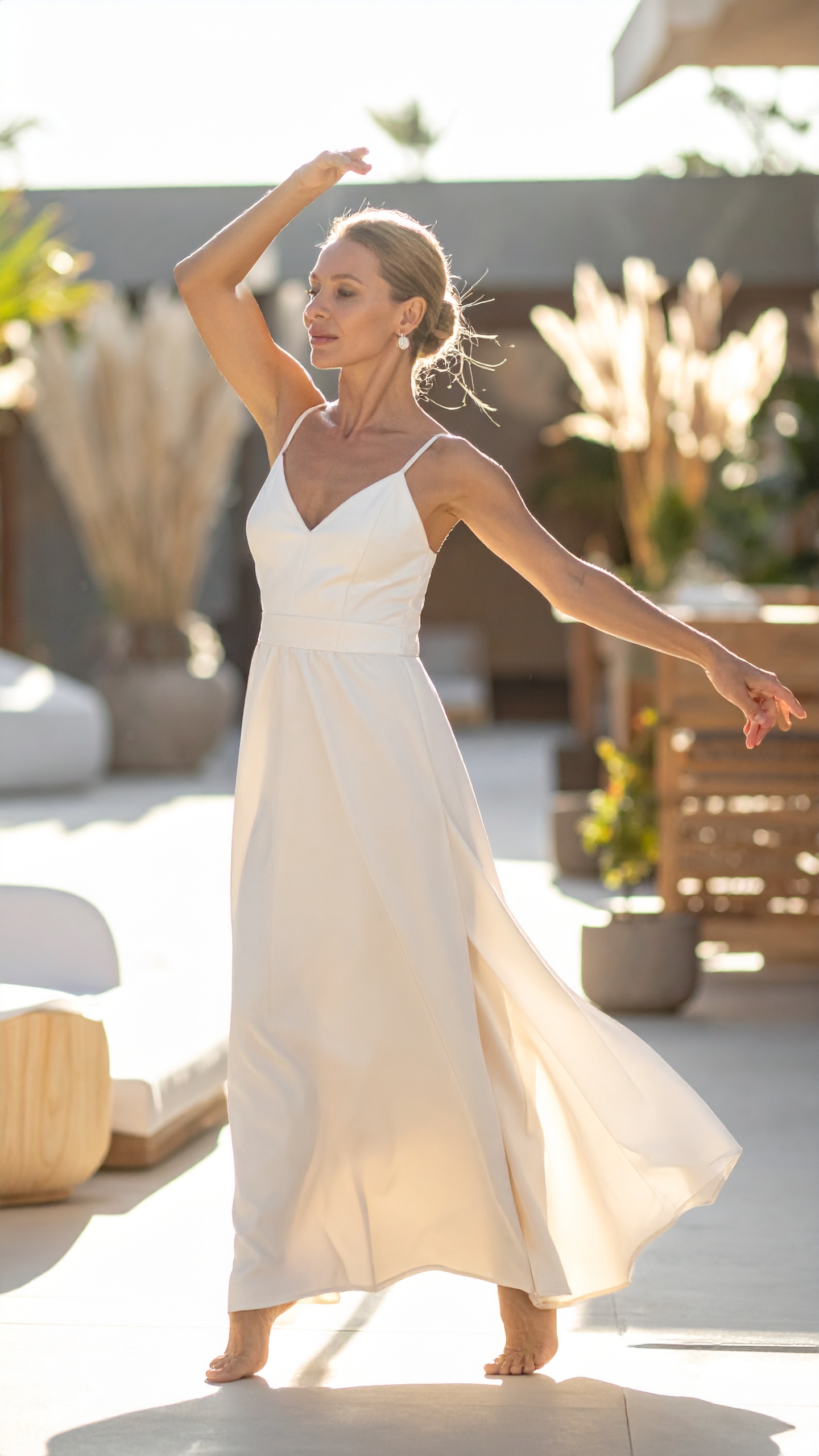 A woman in a long pale gown turning barefoot in low golden light